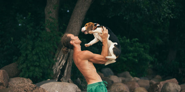 Midsection of shirtless man with woman standing on rock