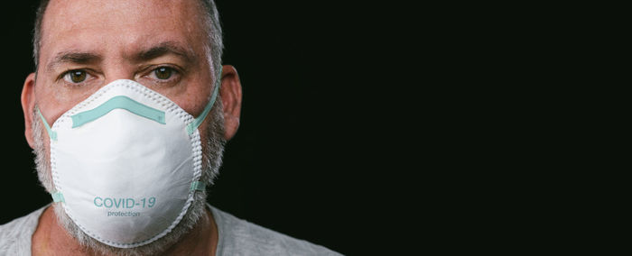 Close-up portrait of man wearing mask against black background