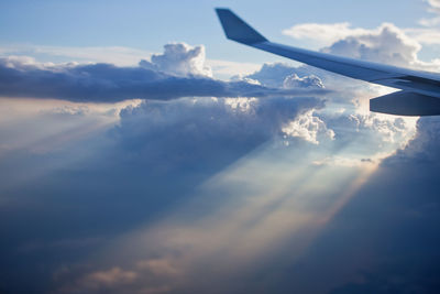 Cropped image of airplane flying by sunbeam streaming from clouds