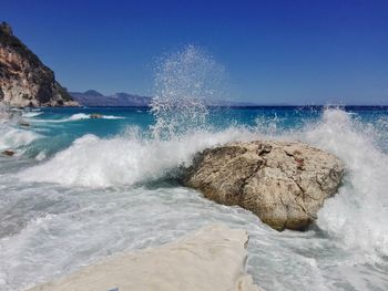 Waves splashing on rocks against clear blue sky