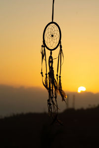 Close-up of silhouette hanging against orange sky