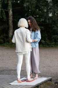 Young beautiful coach helps middle aged woman to stand barefoot on a board with nails. 