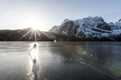 Man ice-skating on frozen lake at sunset
