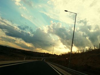 Empty road against cloudy sky at sunset