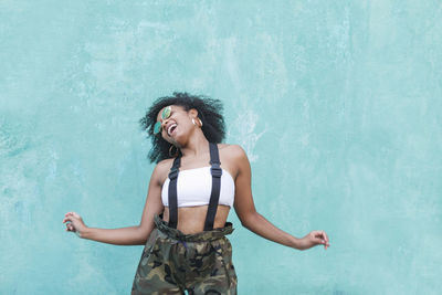 Young woman with curly hair dancing against wall