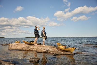 Men standing on rocks near kayaks and looking at sea