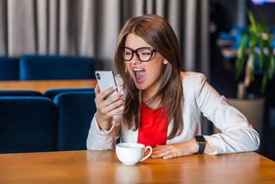 Portrait of young woman using phone while sitting on table