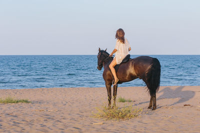 Beautiful woman in white dress riding a horse on the beach at sunset