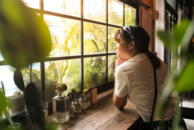 Side view of woman looking through window