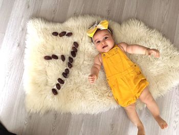 Directly above shot of cute baby girl lying on fur carpet by dates at home