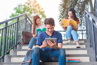 Low angle view of friends studying while sitting on steps in city