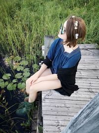 Young woman sitting on wood against plants