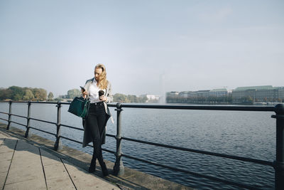 Full length of entrepreneur using mobile phone while standing against sea in city