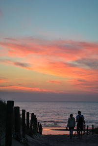 Silhouette people on beach against sky during sunset