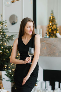 Stylish young woman in a black dress holds a glass of champagne in her hands and celebrates