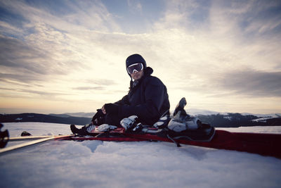 Portrait of skier sitting on snowy landscape against sky