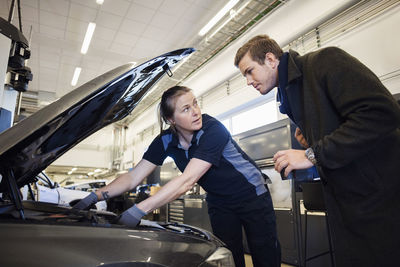 Female mechanic repairing car while looking at customer in auto repair shop