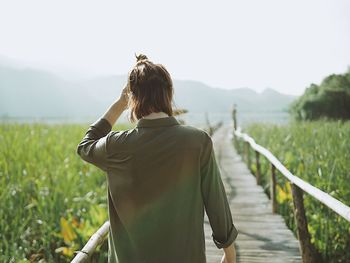 Rear view of woman standing on boardwalk amidst agricultural field