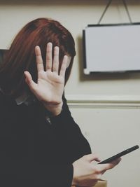 Close-up of teenage girl using phone while showing stop gesture