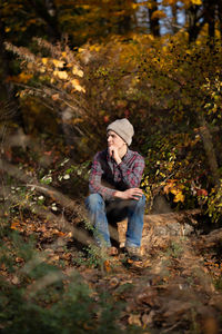 Teen boy sits alone on log in woods looking out thoughtfully.