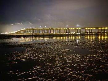 Illuminated bridge over sea against sky at night