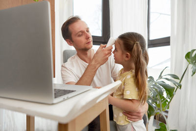 Father measuring temperature of ill daughter at home