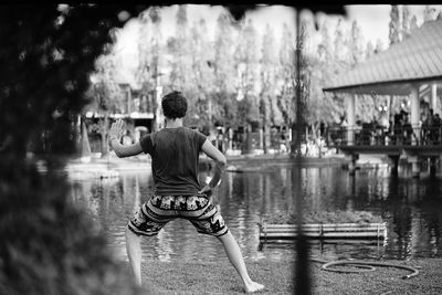 Rear view of young man exercising by pond in park