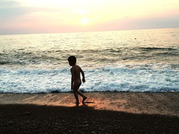 Shirtless boy walking on shore at beach during sunset