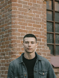 Portrait of young man standing against brick wall