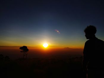 Silhouette man standing on landscape against sky during sunset