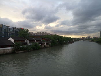 Houses by river against sky at sunset