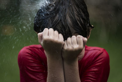 Wet boy covering face from falling water