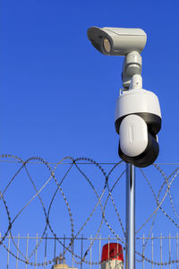 Low angle view of security camera on pole against blue sky