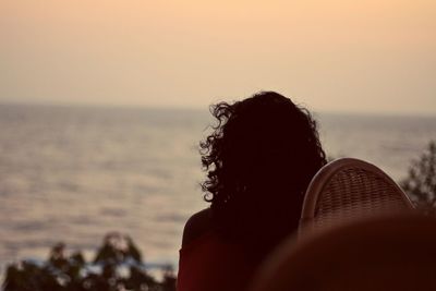 Rear view of woman sitting on chair at beach against clear sky