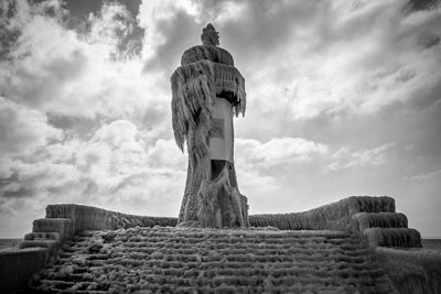 Low angle view of frozen statue and fountain against cloudy sky