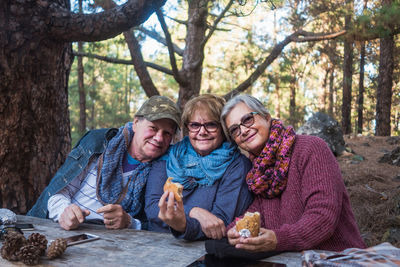 Portrait of happy friends eating food at table in forest