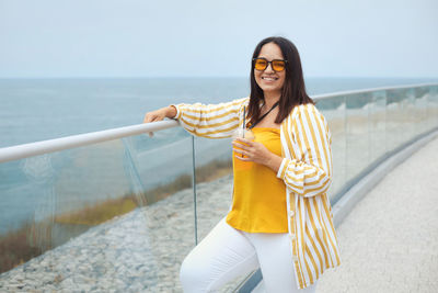 Portrait of smiling woman holding juice standing by railing