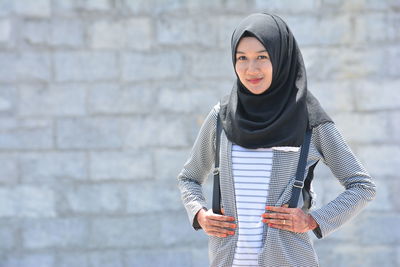 Portrait of smiling woman wearing hijab while standing against wall