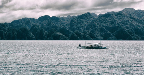 Boat sailing on sea against mountains