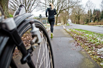 Rear view of woman jogging on road with bicycle wheel in foreground