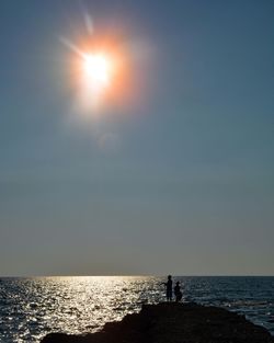 Silhouette person standing on sea shore against sky