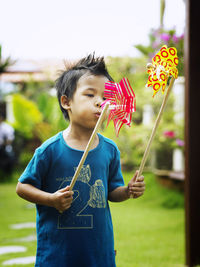 Boy blowing pinwheel toys while standing in yard