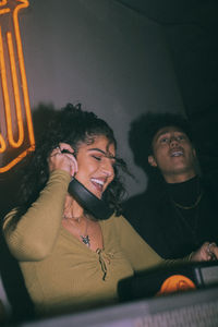 Cheerful young female dj holding headphones by friend dancing at nightclub
