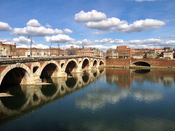 Arch bridge over river by buildings against sky