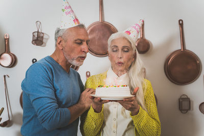 Senior couple holding birthday cake standing in kitchen
