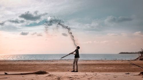 Mature man playing with sand at beach against sky during sunset