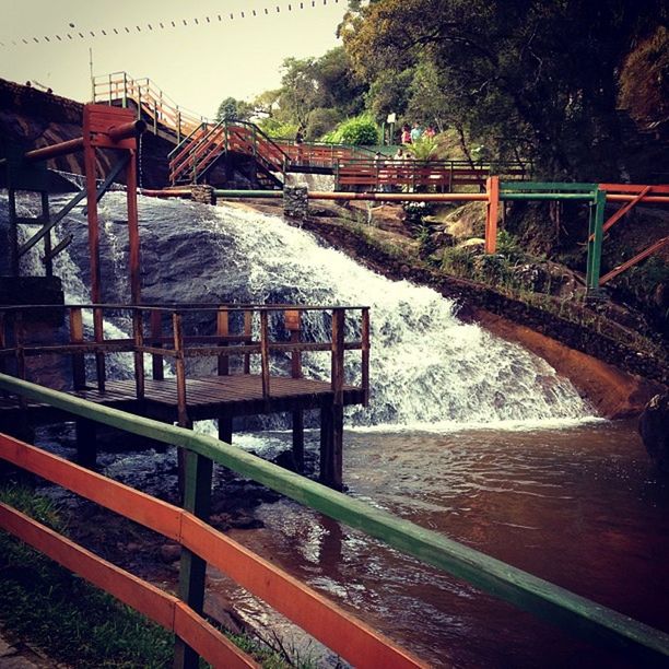 water, bridge - man made structure, connection, river, railing, transportation, tree, built structure, bridge, architecture, footbridge, canal, clear sky, engineering, day, nature, outdoors, lake, arch bridge, metal