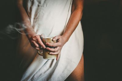 Midsection of woman holding coffee over black background