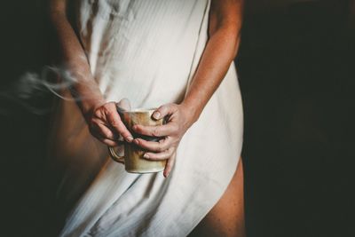 Midsection of woman holding coffee over black background