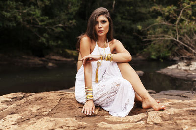 Young woman wearing dress sitting on rock formation at forest